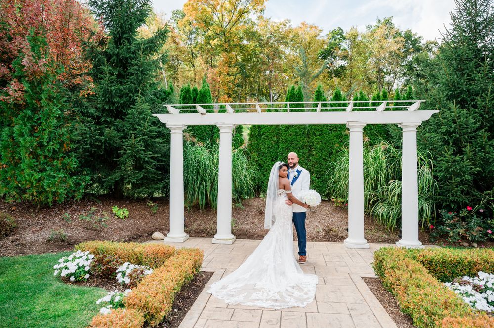 A romantic garden scene with a white pergola and stone pathway surrounded by lush greenery and colorful foliage.