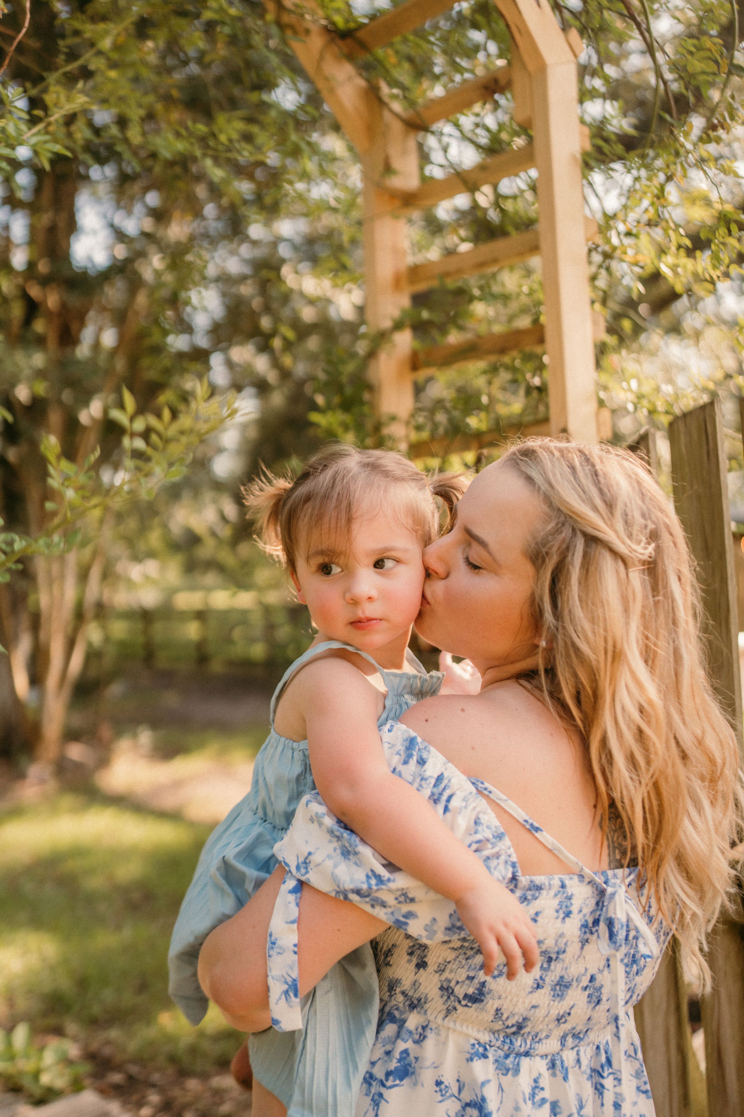 Mother and child share a tender moment together in a sunlit garden surrounded by trees.