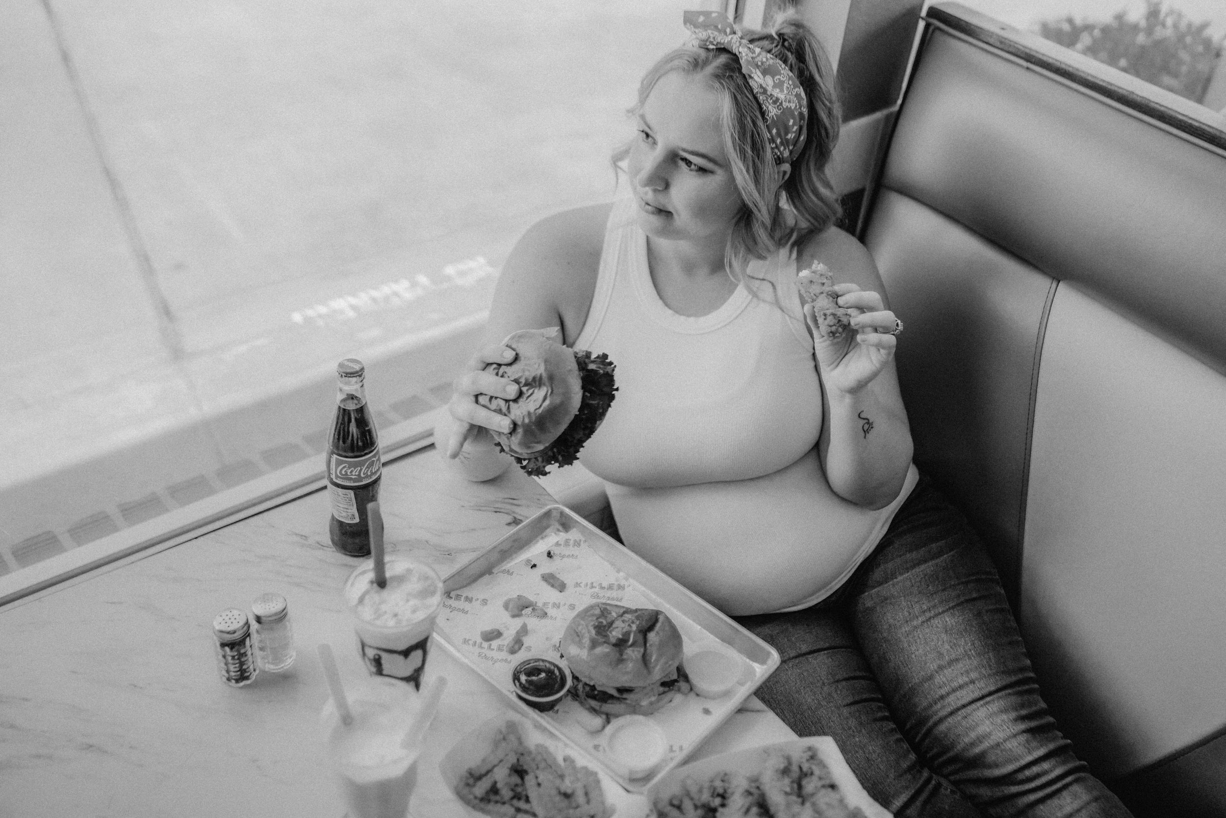 Woman enjoying a casual meal alone in a diner booth with drinks and food on the table.