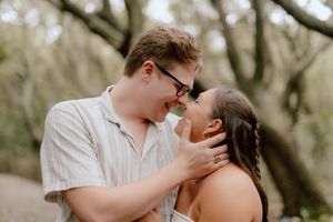 A romantic couple shares tender moments in a natural outdoor setting with trees and soft lighting.