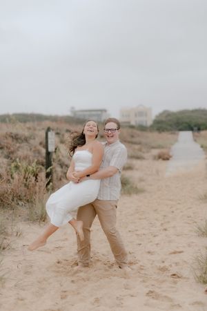 A couple shares a romantic moment on a sandy beach path surrounded by coastal vegetation.