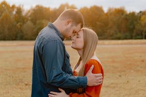 A couple embraces in a golden autumn field during sunset, creating a romantic silhouette against the warm sky.