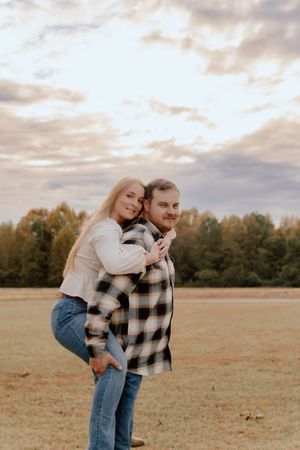 A couple shares an intimate moment in a golden autumn field at sunset while wearing casual denim and plaid clothing.