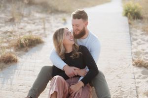 A romantic couple shares laughter while sitting together on sandy dunes.