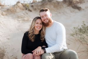 A couple in contrasting black and white outfits embrace while sitting on sandy terrain.