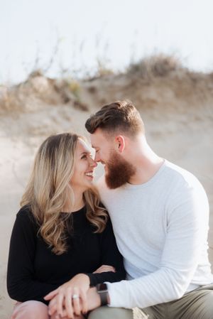 A couple shares an intimate moment sitting together against a sandy backdrop.