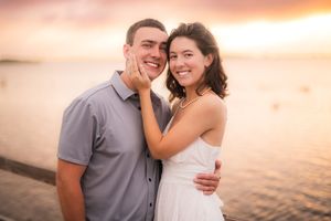 A happy couple embraces at sunset by the water, smiling warmly as they share an intimate moment together.