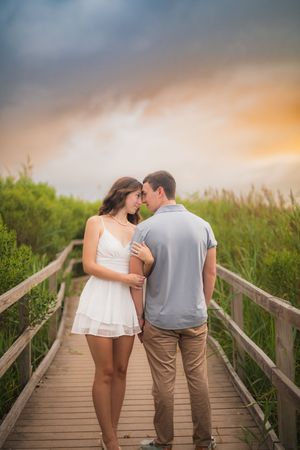 Romantic couple walking on a wooden boardwalk through tall grass at sunset with golden light.