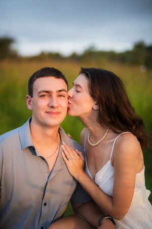 A romantic moment captured outdoors with a couple sharing a tender kiss in a sunlit field at dusk.