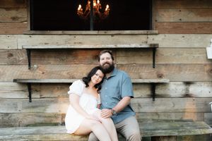Couple sitting together on rustic wooden steps in front of a reclaimed wood wall with a chandelier above.