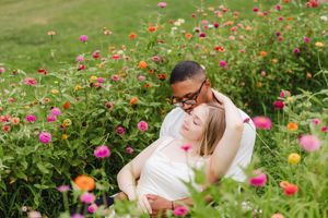 Couple embracing romantically among vibrant pink, orange, and red zinnia flowers in a lush green garden.