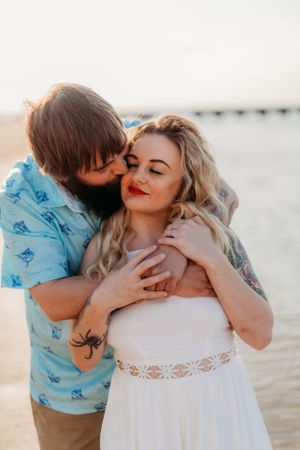 A loving couple embraces on the beach during a sunset photoshoot.