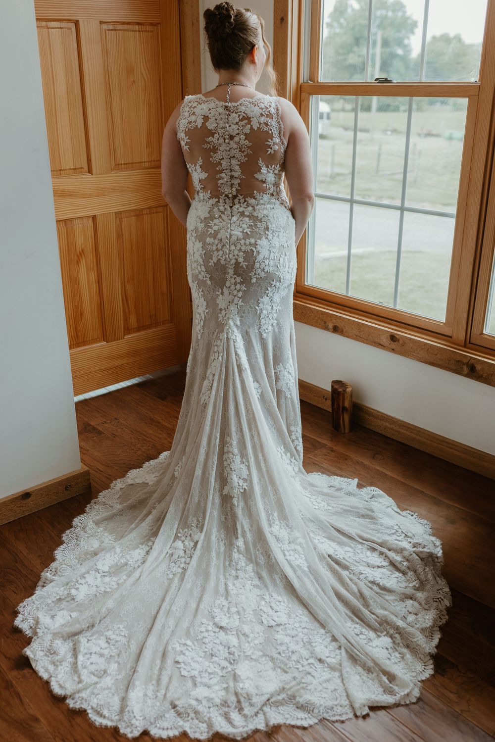 Elegant lace wedding dress with detailed back and flowing train on hardwood floor.
