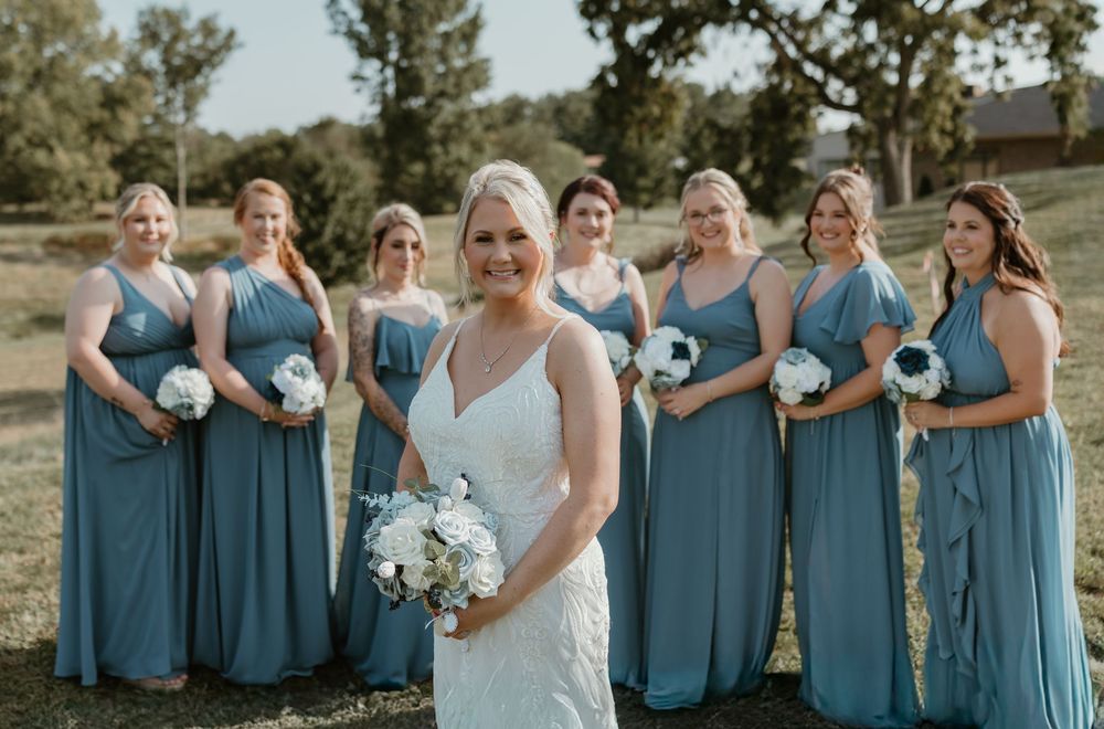 Bridesmaids wearing matching dusty blue dresses holding white bouquets.