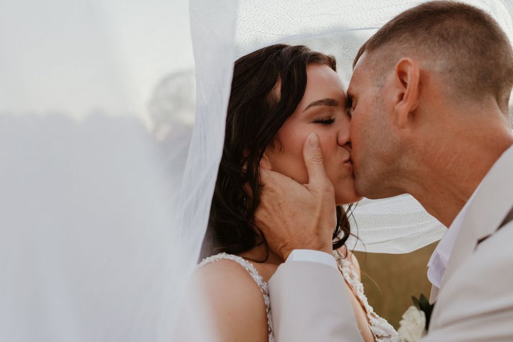 Close-up of newlyweds sharing their first kiss under white veil.