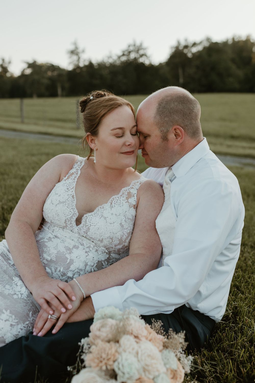 Couple sharing intimate moments while sitting in grassy field with bouquet.