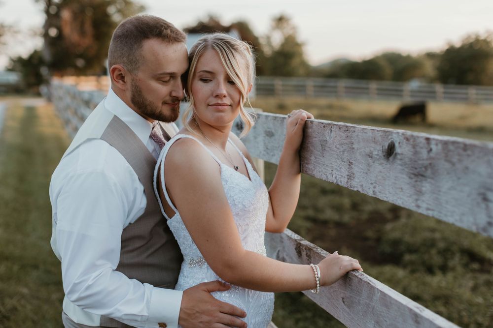 Candid wedding photography showing tender moments between newlyweds by a rustic fence.