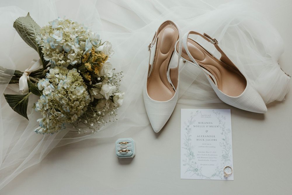 Wedding details flatlay with flowers, shoes and invitations on white background.