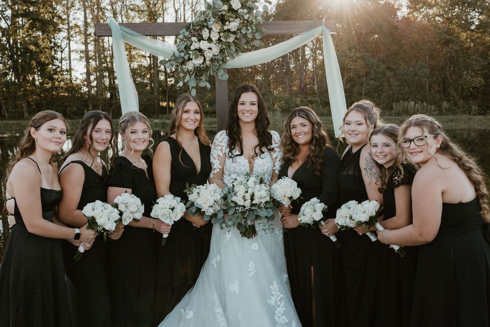 Bridal party in black dresses poses with bride holding white bouquets.