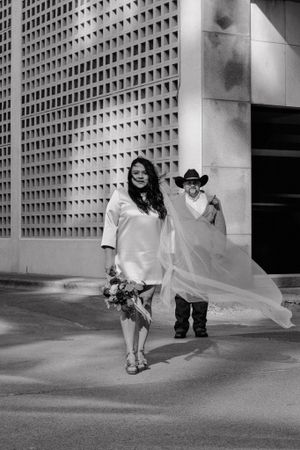 A black and white wedding photo of a couple posing against a geometric wall with flowing veil.