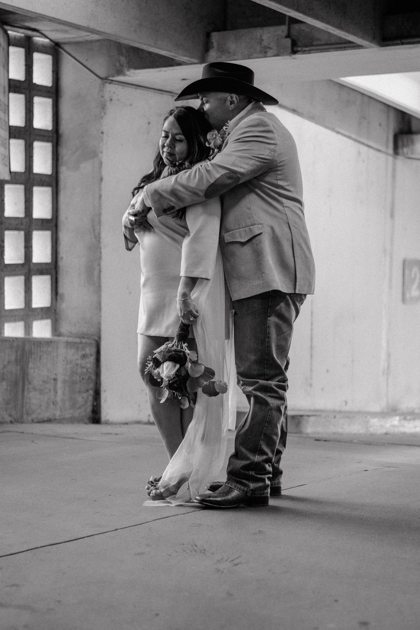 A tender black and white portrait of a couple embracing in a modern architectural setting.