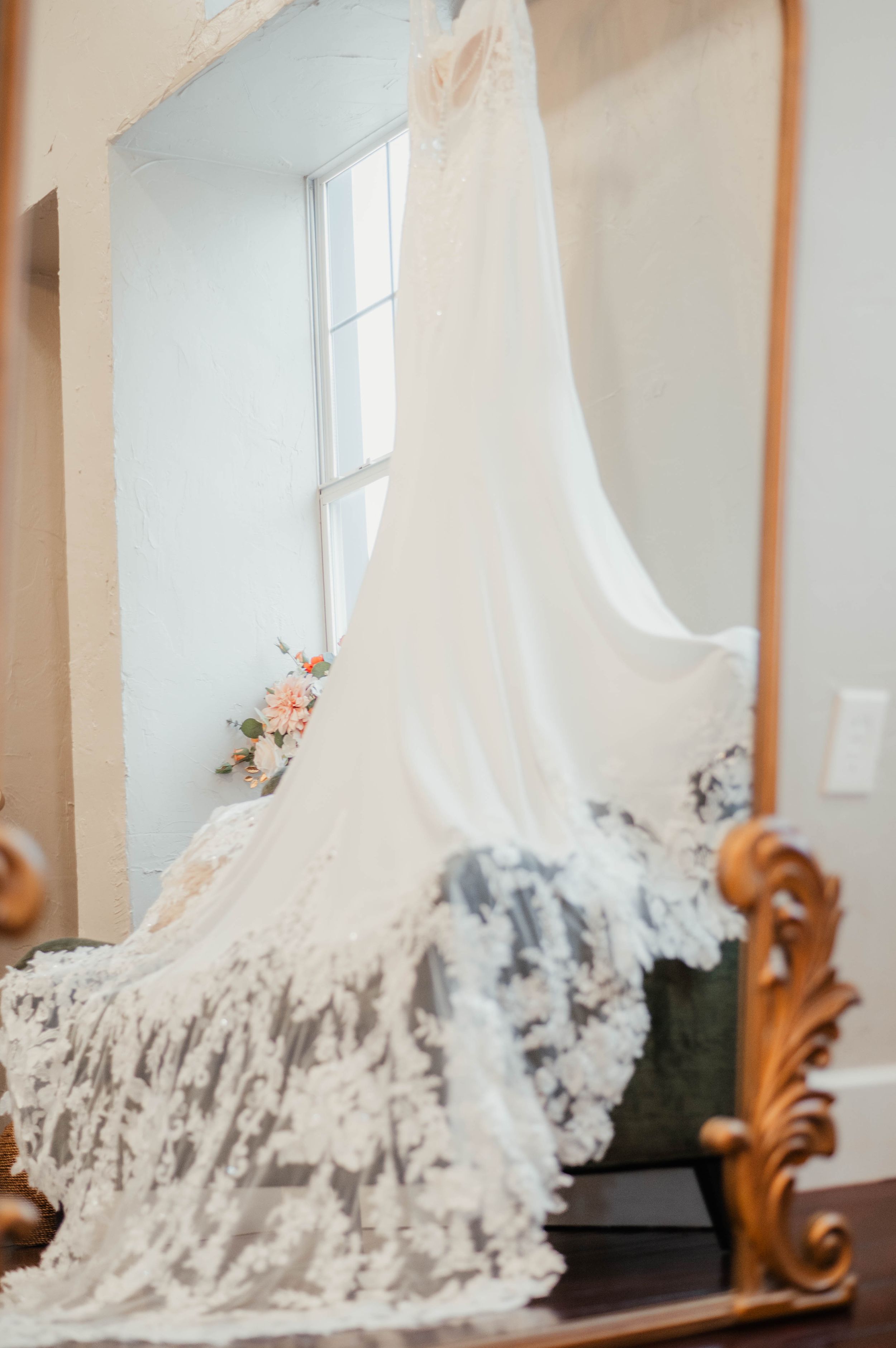 An elegant lace wedding dress with long train displayed in a mirror reflection.