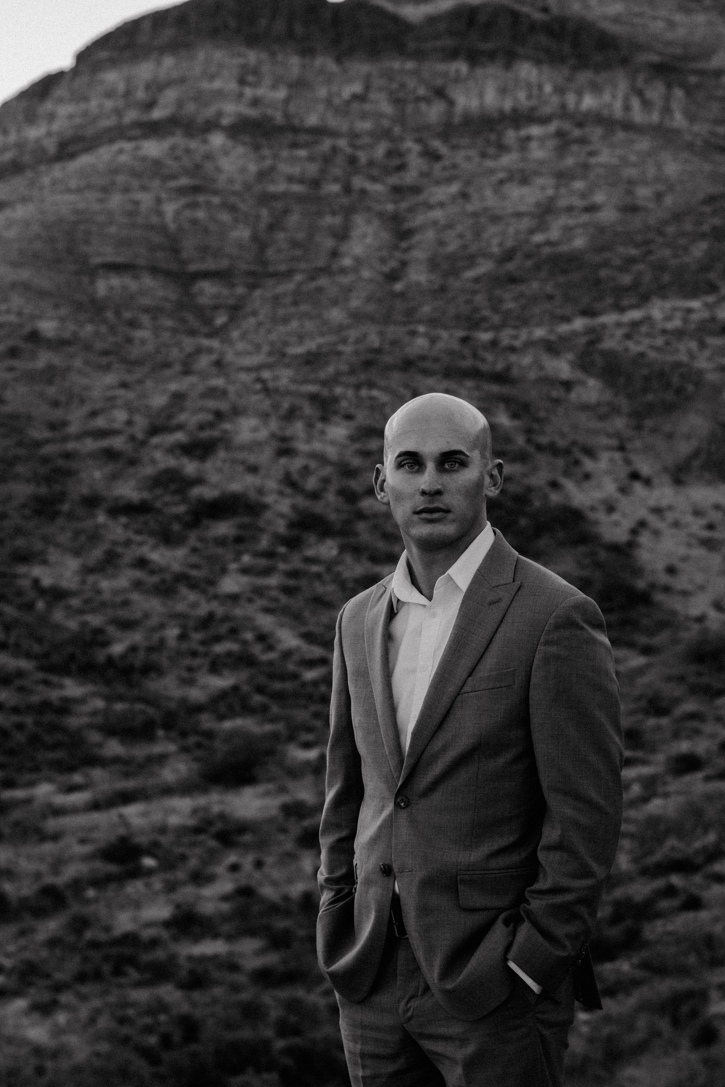 A portrait against a dramatic mountain backdrop wearing a tailored suit.