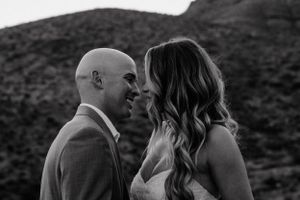 Black and white wedding photo showing intimate moment between couple against mountainous backdrop at sunset.