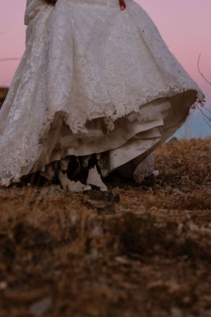 Close-up detail shot of lace wedding dress hem against dusty ground.