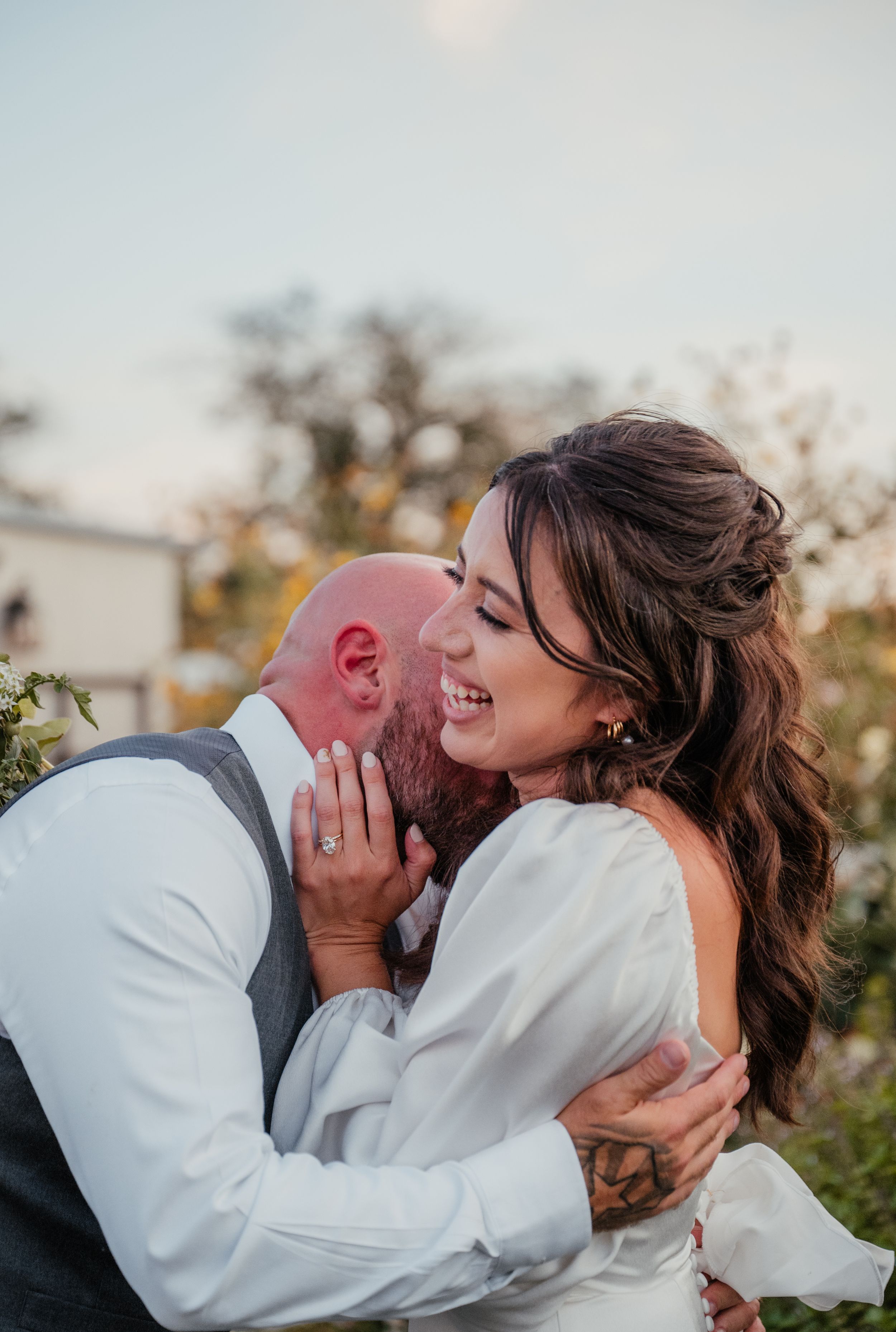 A joyful couple shares an intimate moment outdoors during their wedding celebration at sunset.