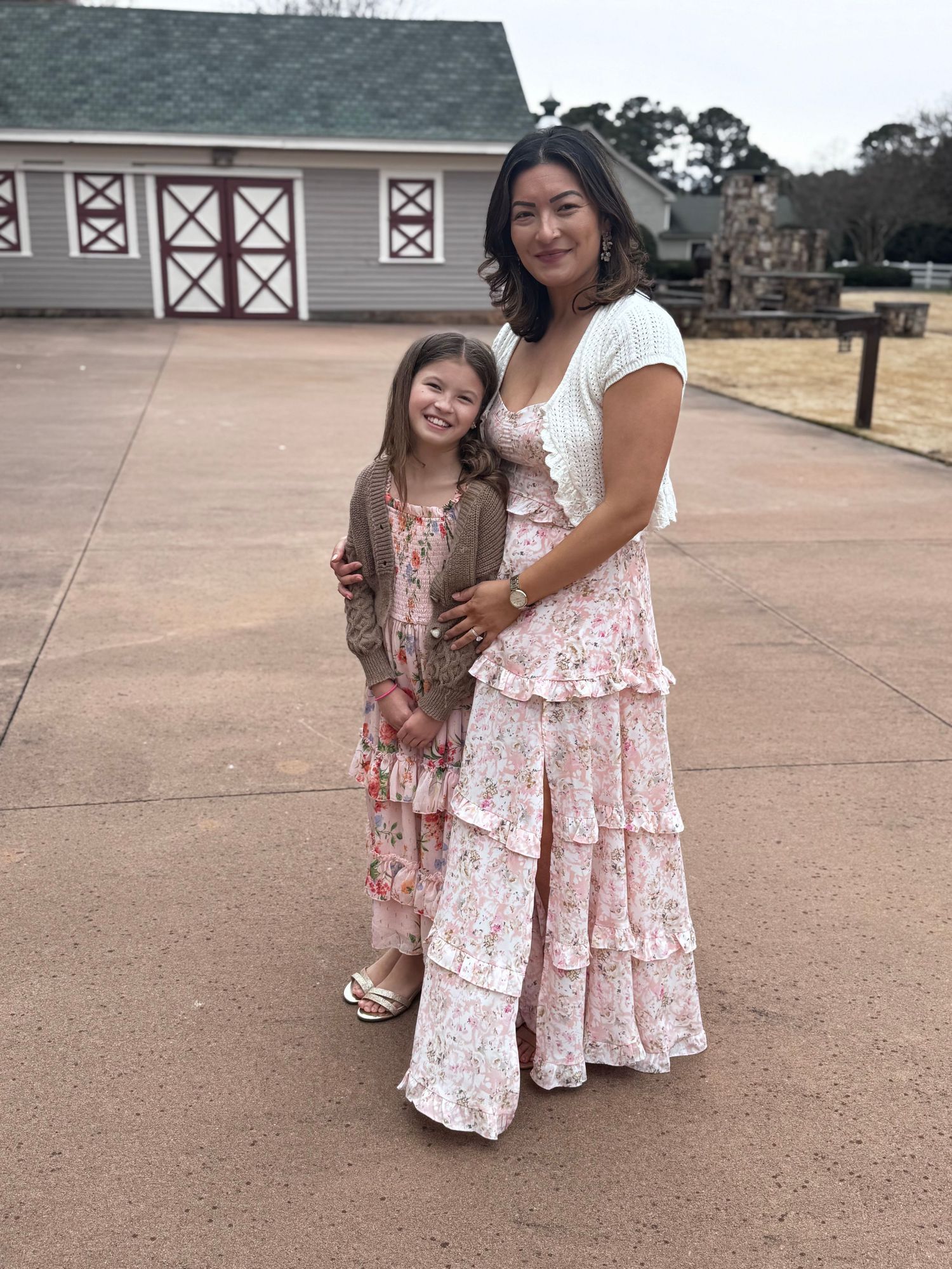Two people wearing coordinating pink floral dresses stand together on a concrete patio.