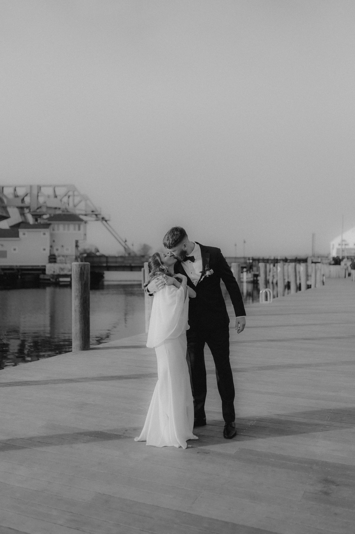 An intimate pose against a light gray wall showcasing a lace wedding dress and gray suit.