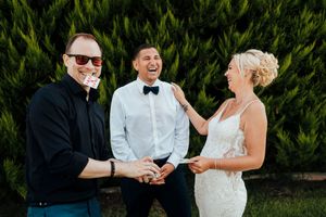 A couple shares a joyful moment during their wedding reception outdoors with lush greenery in the background.