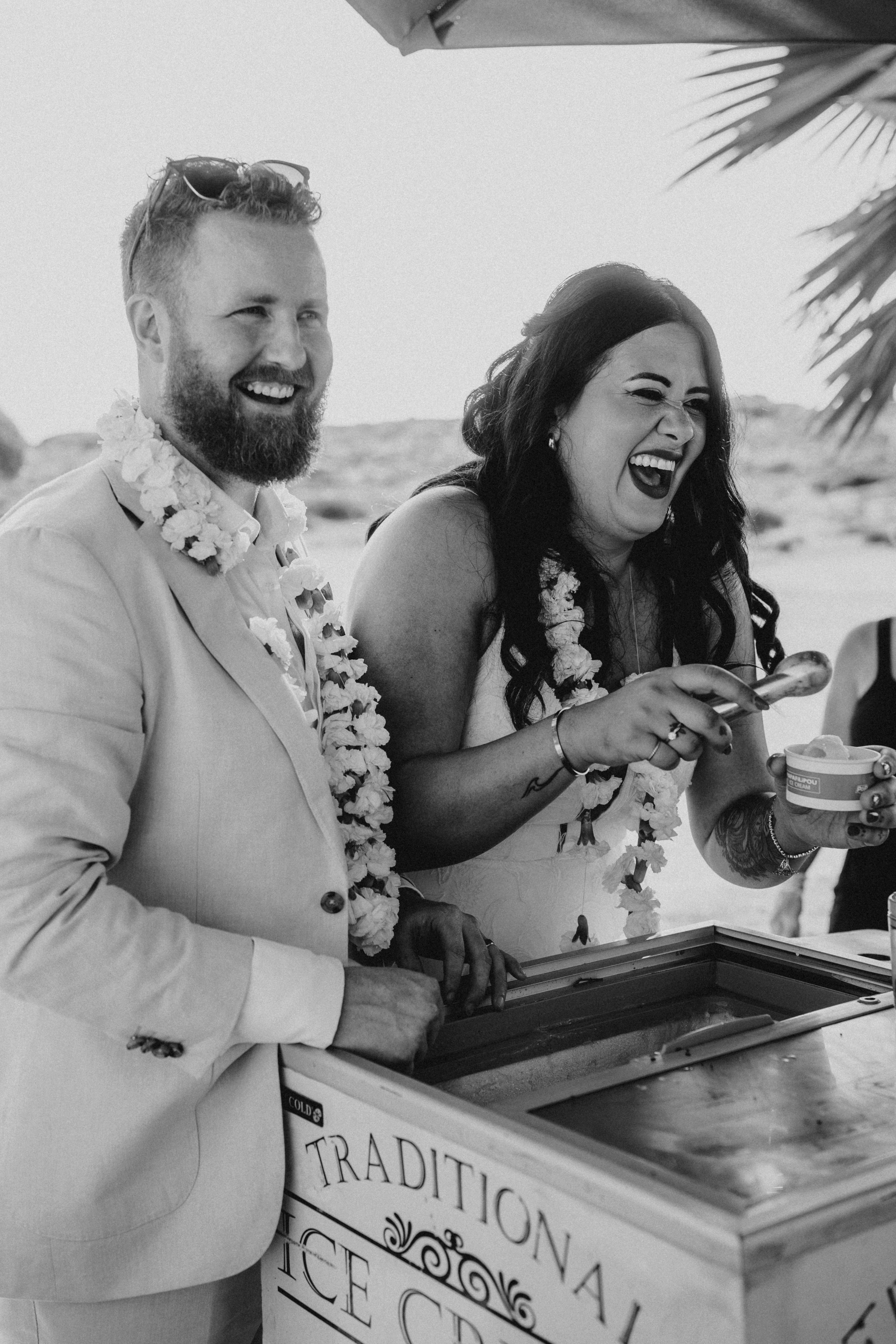 A joyful couple laughs together while signing documents at a wedding ceremony outdoors.