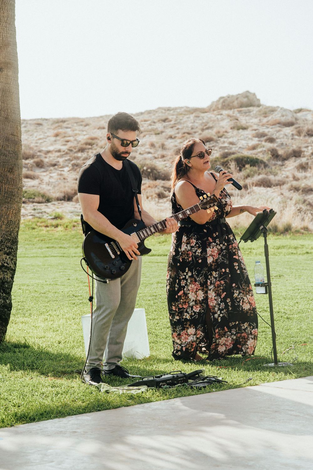 Musicians perform on a sunny outdoor patio with desert landscape and mountains visible in the background.