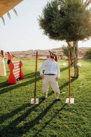 Outdoor lawn game setup with wooden posts and shovels at a desert venue with people in formal attire.