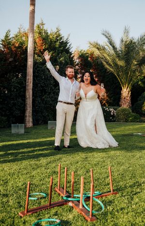 Couple plays lawn games with ring toss at an outdoor wedding reception in a palm tree garden setting.
