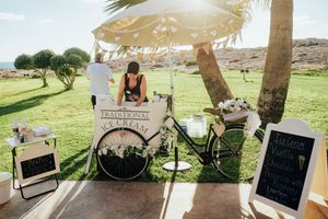 A rustic outdoor wedding ceremony setup with chalkboard signs and floral decorations under palm trees at sunset.