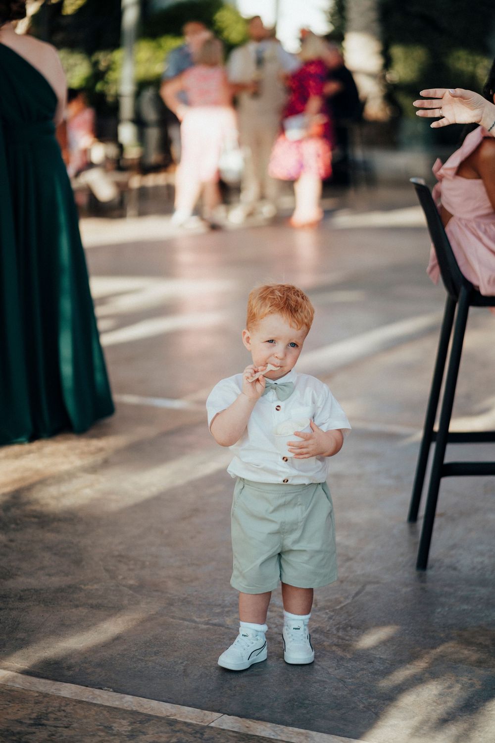 A toddler in mint green shorts and white shoes plays on a sunlit outdoor patio.