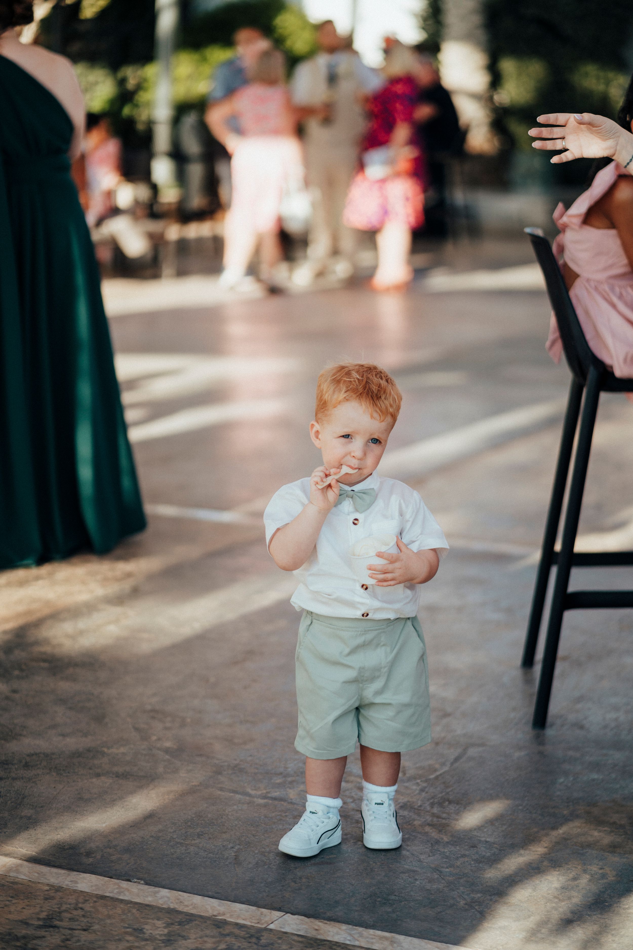 A toddler in mint green shorts and white shoes plays on a sunlit outdoor patio.