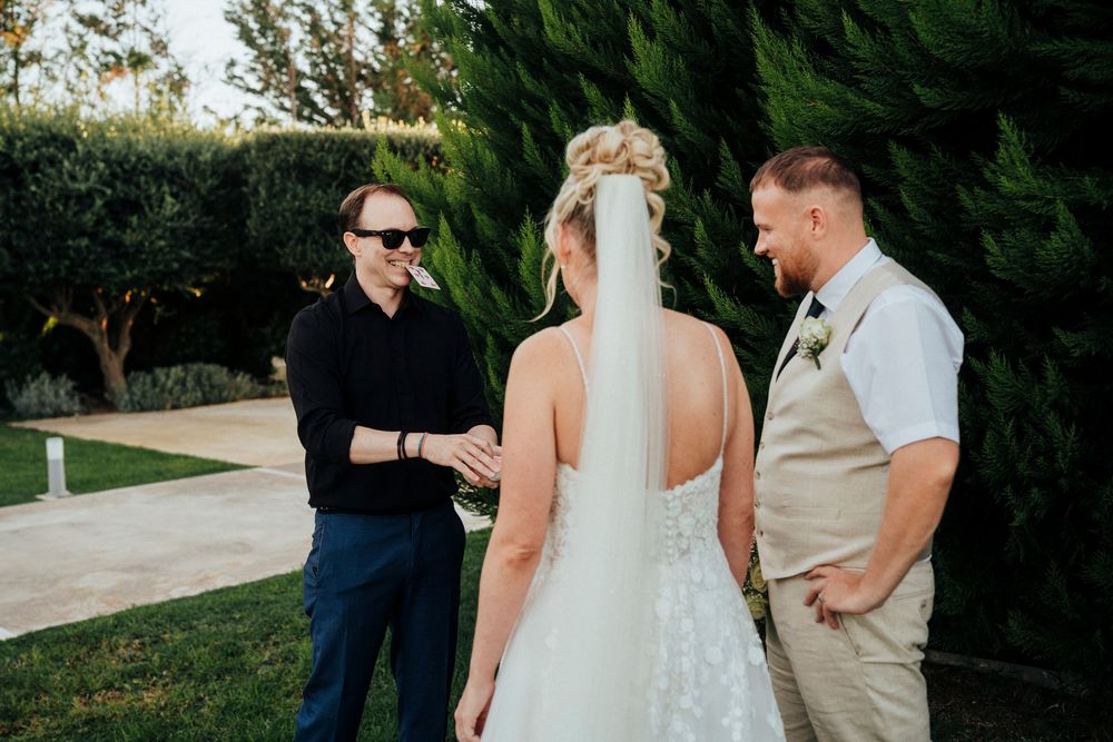 An outdoor wedding ceremony takes place in a garden setting with three people gathered together at sunset.