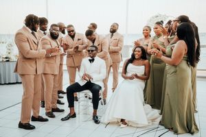 Wedding party in tan suits and sage green dresses poses together on rooftop during celebration.