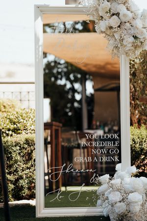 Elegant wedding reception decor featuring white-framed glass signs with calligraphy text and floral arrangements.