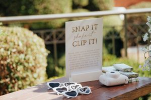 Wedding reception table with 'Snap It Clip It' sign, disposable cameras and heart-shaped sunglasses for guests.