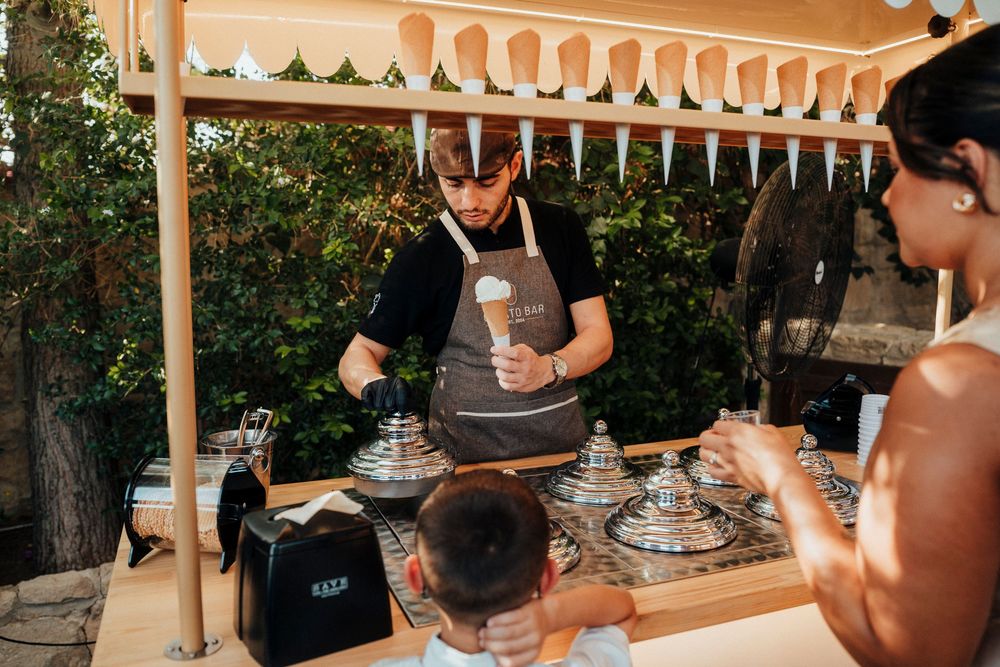 Barista preparing coffee drinks at an outdoor coffee bar with a wooden awning and lush greenery in the background.