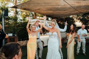 Wedding party celebrates on outdoor dance floor under canopy during sunset reception at garden venue.