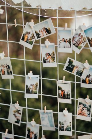 Multiple polaroid photos hanging on strings against a blurred natural background create a decorative display wall.