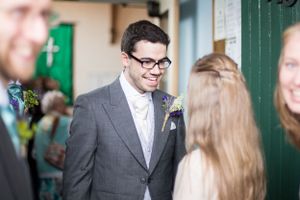 A wedding guest in a grey suit and glasses mingles during the celebration.