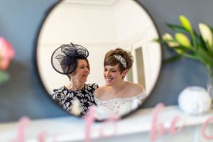 Mirror reflection shows two elegantly dressed women sharing a happy moment.