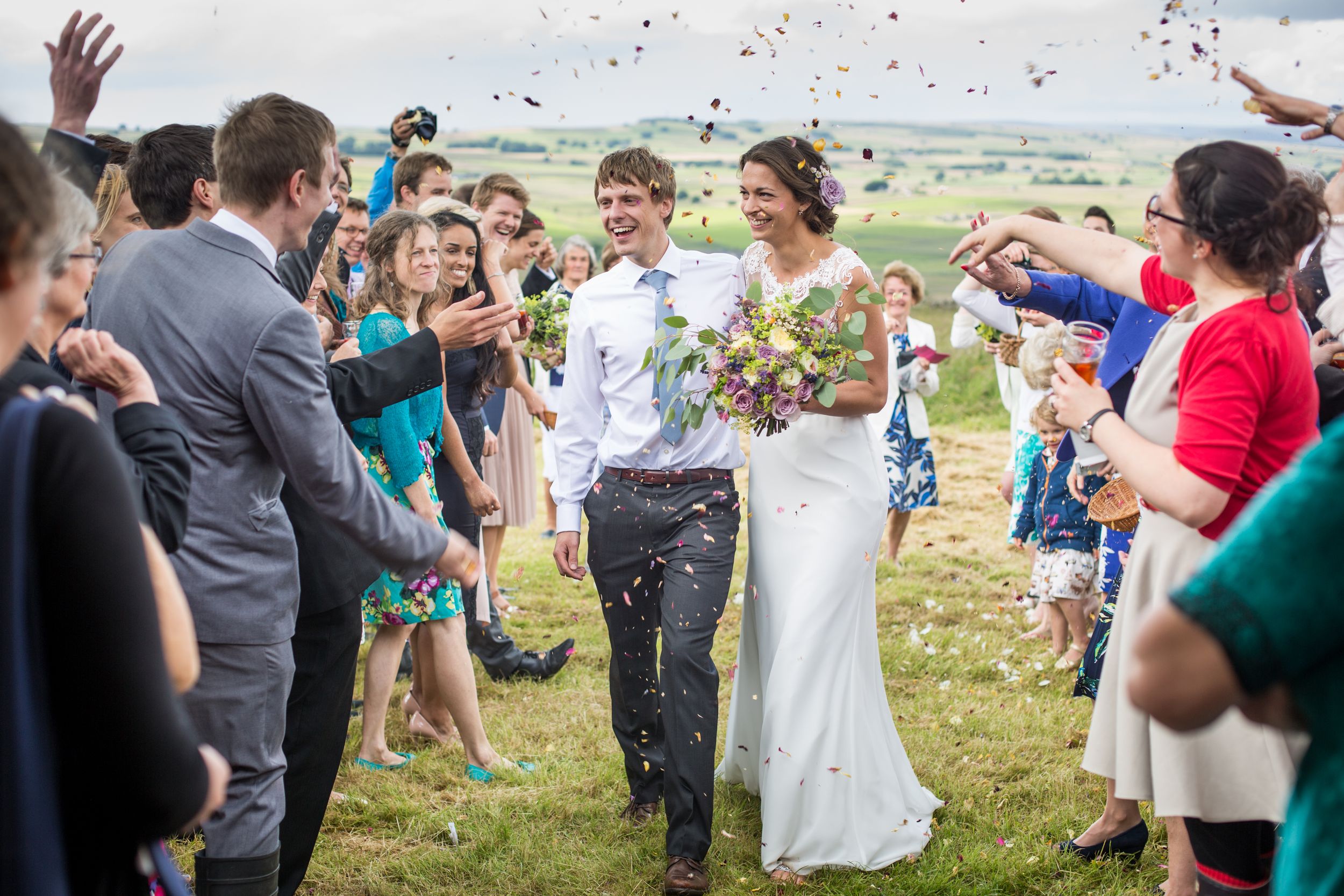 Wedding guests shower the happy couple with confetti on a scenic hilltop.